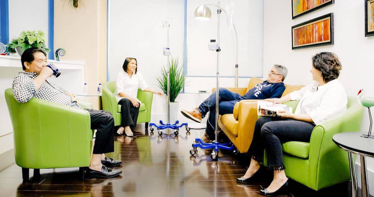 Four people are relaxing in a specialty infusion center while receiving IV infusion therapy